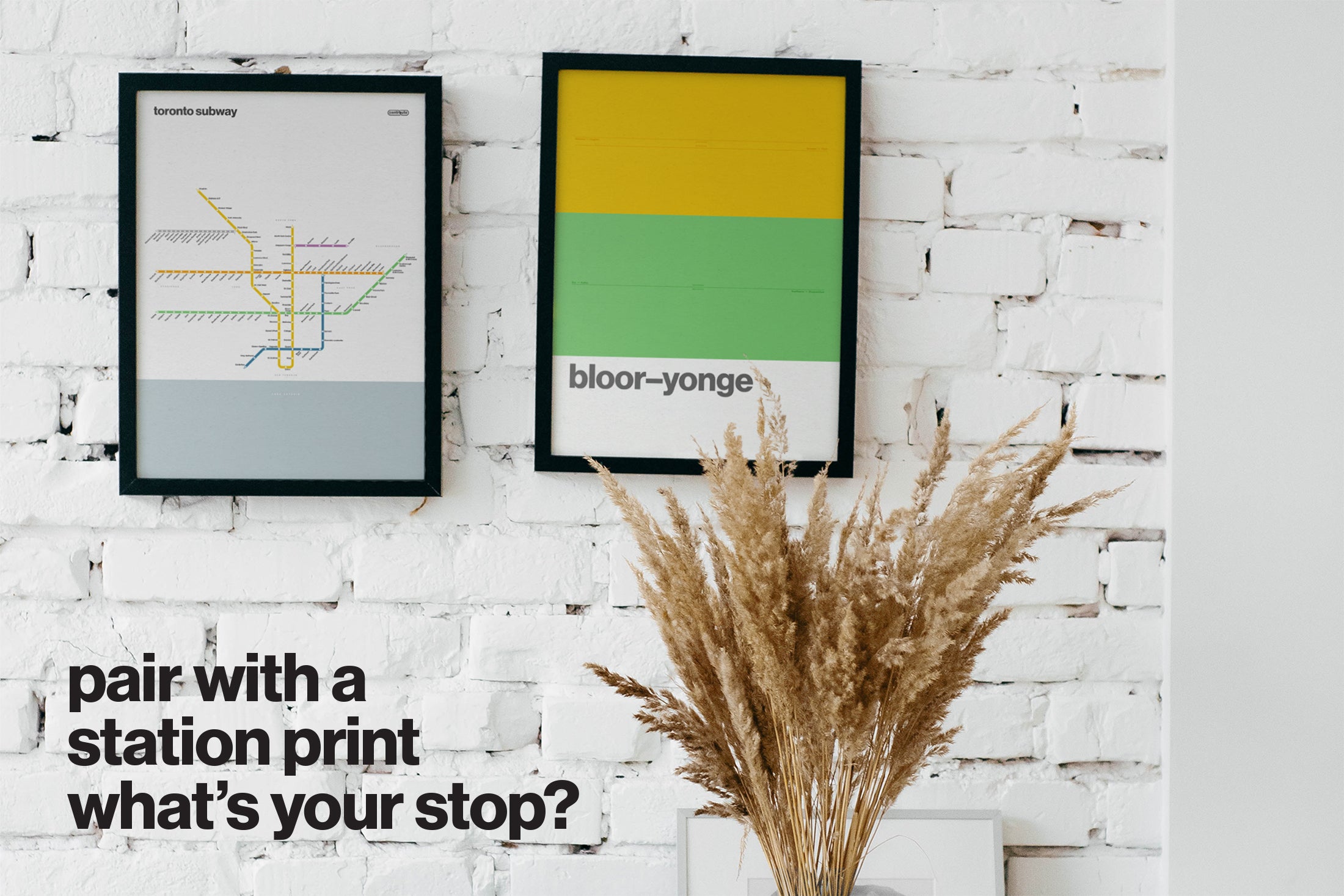 a white brick wall with two framed prints hanging on it, one depicting a subway map and the other a colorful abstract design. There is also a vase of dried grasses placed on the wall. The text at the bottom of the image reads "Is with a station print what's your stop?"